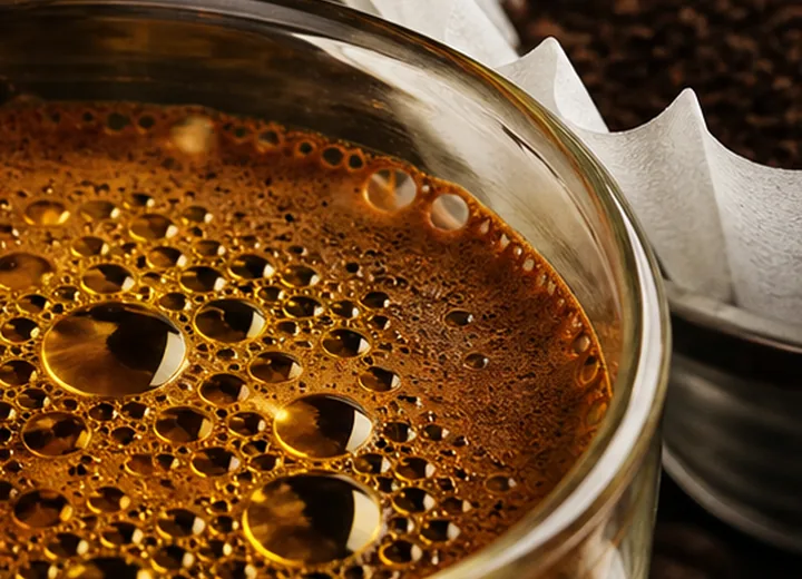 Macro espresso surface with shimmering coffee oils beside a paper filter