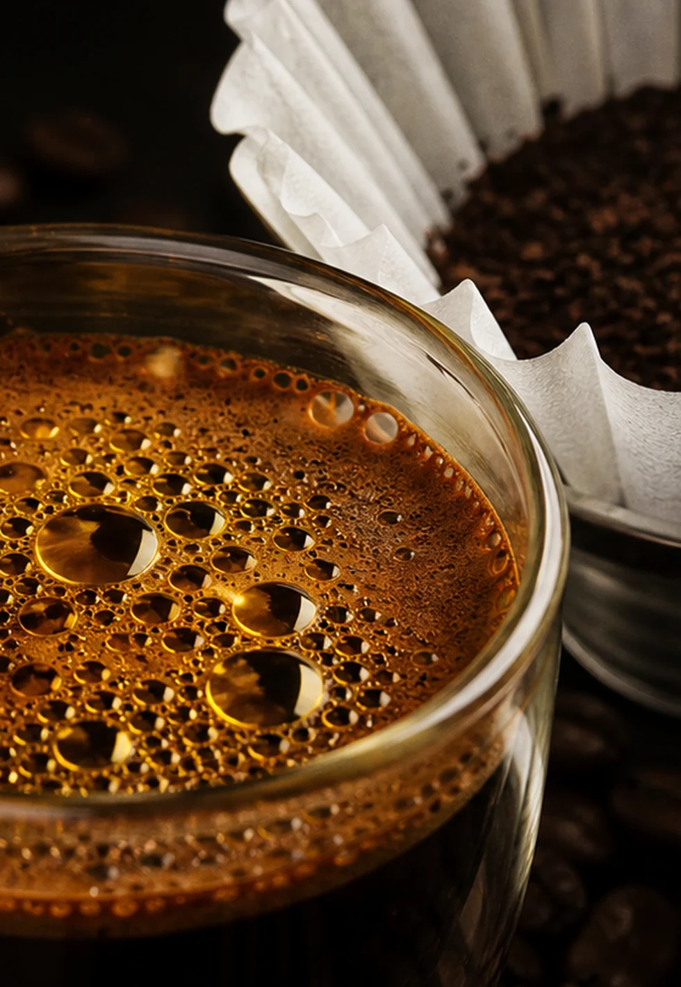Macro espresso surface with shimmering coffee oils beside a paper filter