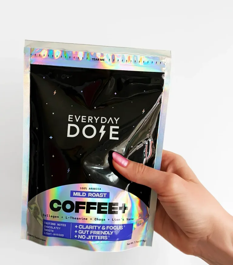 A hand holding Everyday Dose Mild Roast Coffee+ in its black and holographic 219 g pouch
