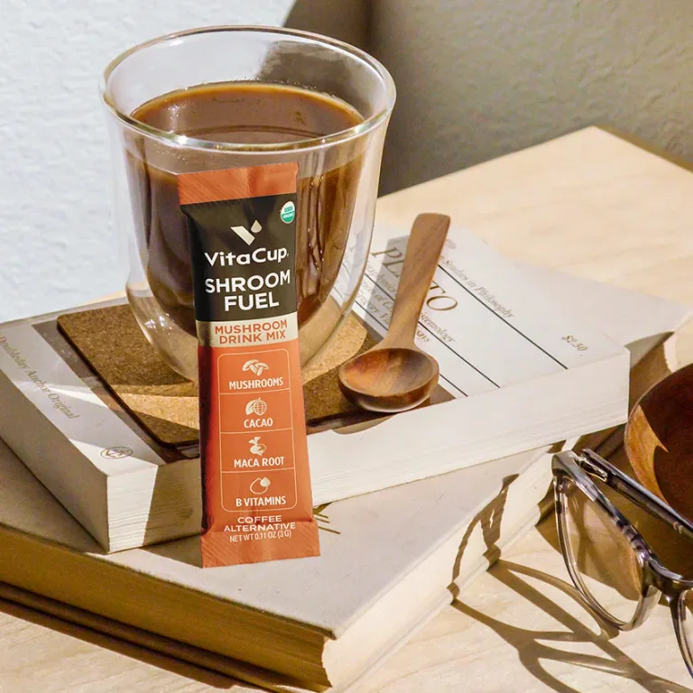 A VitaCup Shroom Fuel coffee-alternative single-serve stick beside a prepared drink on a wooden tray