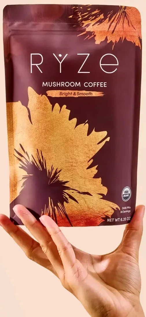 A hand holding a photographed RYZE Medium Roast Bright and Smooth Mushroom Coffee 30-serving pouch